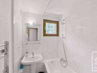 This bright and clean bathroom features a pedestal sink, a bathtub with a shower, and a small window offering natural light.