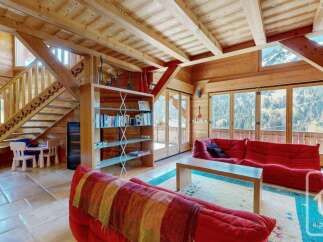 Experience the charm of this rustic wooden chalet, featuring a cozy living area with plush red sofas and a vibrant striped throw.