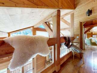Experience rustic charm in this wooden chalet, featuring a cozy loft space with plush sheepskin throws and stunning mountain views through large windows.