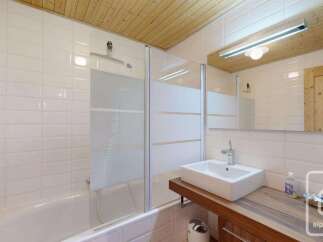 This modern bathroom features a sleek white bathtub with a glass shower enclosure, complemented by white subway tiles and a wooden ceiling.