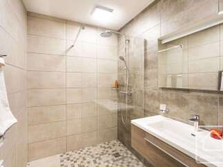 Experience modern comfort in this beautifully tiled bathroom, featuring a spacious walk-in shower with a rainfall showerhead and a sleek vanity with a vessel sink.