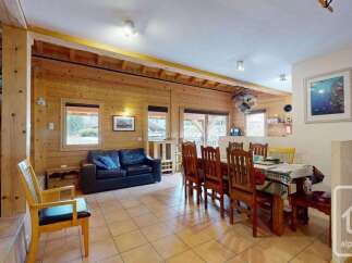 Experience rustic charm in this spacious wooden chalet, featuring a cozy living area with a black leather sofa and a large dining table perfect for gatherings.