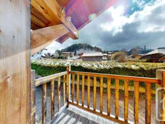 Experience the charm of this alpine property with its rustic wooden balcony offering scenic views of the surrounding village and snow-dusted hills.