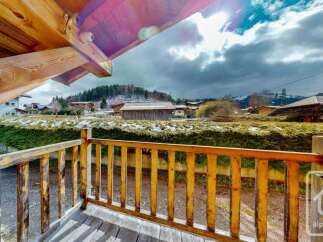 Experience the charm of this alpine property, featuring a rustic wooden balcony with scenic views of the surrounding village and snow-dusted hills.