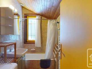 This charming bathroom features a bathtub with a white shower curtain, a wooden ceiling, and tiled walls.