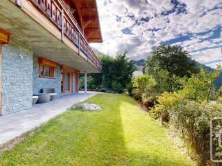 Experience luxury mountain living with this stunning property featuring a stone facade and a spacious wooden balcony overlooking a lush green lawn.