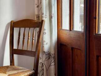 Experience rustic charm with this inviting wooden chair featuring a woven seat, perfectly complementing the natural light filtering through the patterned curtains.