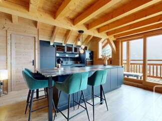 Experience modern alpine living in this stunning kitchen and dining area, featuring a sleek dark island with bar seating and a backdrop of exposed wooden beams.