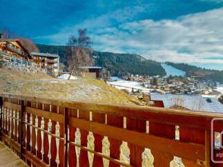 Enjoy breathtaking mountain views from this charming property, featuring a rustic wooden balcony overlooking a snow-dusted village and ski slopes.