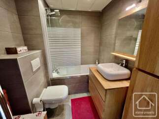 This modern bathroom features a sleek design with large grey tiles and a freestanding white sink atop a wooden vanity.