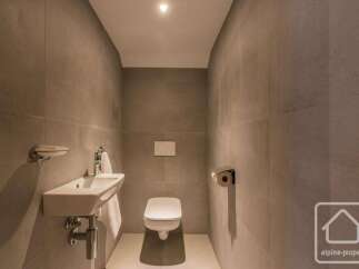 This modern bathroom features a sleek white sink with chrome fixtures, complemented by a wall-mounted soap dispenser and a neatly folded white towel.
