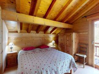 Experience rustic charm in this cozy alpine bedroom, featuring a comfortable double bed adorned with a charming polka dot duvet and plush red pillows.
