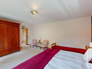This spacious bedroom features a large wooden wardrobe and a comfortable bed adorned with a rich burgundy throw.