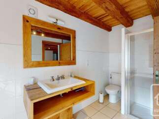 This charming bathroom features a rustic wooden vanity with a white ceramic sink, complemented by exposed wooden ceiling beams that add warmth and character.