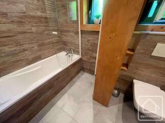 Experience modern comfort in this stylish bathroom featuring a sleek bathtub with a glass enclosure and wood-effect tiling.