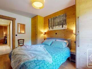 Experience cozy mountain living in this charming bedroom featuring warm wood paneling and a comfortable bed adorned with blue patterned bedding.