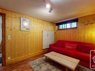 Experience cozy living in this charming room featuring warm wood-paneled walls and a comfortable red sofa.