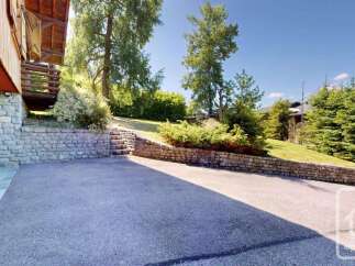 Discover this charming property featuring a rustic stone wall and a paved driveway leading to a traditional wooden house.