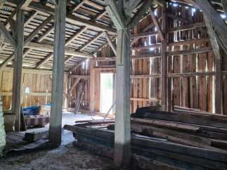 Explore the rustic charm of this spacious barn, featuring robust wooden beams and a corrugated metal roof, offering ample potential for renovation or conversion.