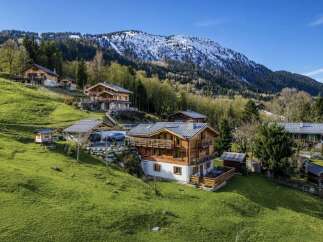 Experience luxury mountain living in this stunning chalet nestled on a verdant hillside with breathtaking views of snow-capped peaks.