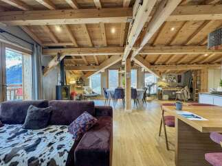 Experience rustic charm and modern comfort in this spacious open-concept living area, featuring exposed wooden beams and a cozy fireplace.