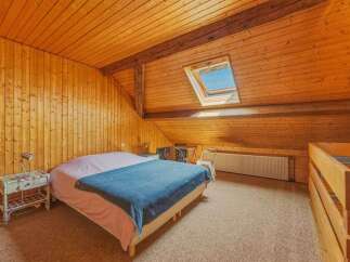 Experience cozy living in this charming attic bedroom, featuring warm wood paneling throughout and exposed beams for a rustic feel.