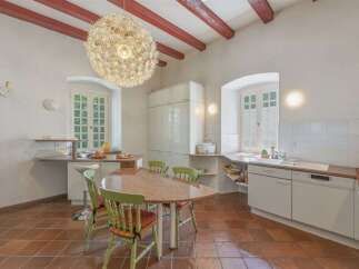 This charming kitchen features a unique dandelion-shaped chandelier hanging from exposed red wooden beams, adding a whimsical touch to the vaulted ceiling.