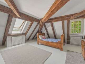 Discover this charming attic bedroom featuring exposed wooden beams and a skylight that floods the space with natural light.