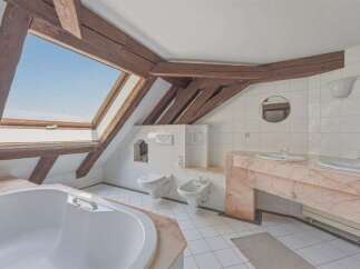 Experience unique charm in this attic bathroom featuring exposed wooden beams and a large skylight offering breathtaking sky views.