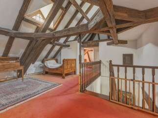 Discover rustic charm in this attic bedroom, featuring exposed wooden beams and a unique triangular skylight that floods the space with natural light.