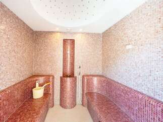Experience ultimate relaxation in this beautifully tiled steam room, featuring comfortable mosaic-covered benches and a central steam generator.