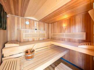 Experience ultimate relaxation in this luxurious wooden sauna, featuring tiered benches for comfortable seating and a traditional bucket with a ladle.