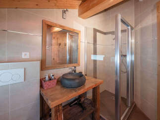 Experience rustic charm in this bathroom featuring a wooden vanity with a stone vessel sink and a modern glass-enclosed shower.