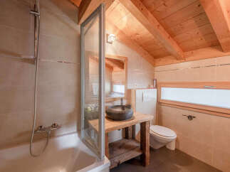 Experience rustic charm in this bathroom featuring a deep soaking tub with a shower, a unique stone vessel sink atop a wooden vanity, and a modern toilet.