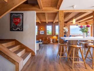 Experience luxurious mountain living in this stunning chalet featuring a modern open-plan living space with a sleek white island bar and comfortable wooden stools.
