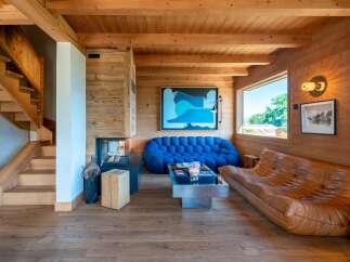 Experience luxury mountain living in this stunning chalet featuring a modern open-plan living area with a cozy fireplace and a striking blue modular sofa.