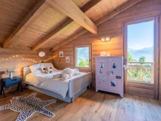 Experience cozy mountain living in this charming attic bedroom, featuring exposed wooden beams and a sloped ceiling that adds character.