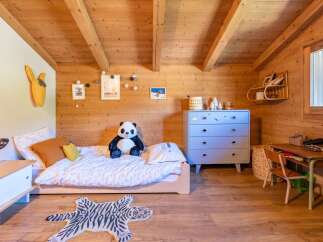 This charming children's bedroom features a cozy wooden interior with a single bed adorned with playful bedding and a large panda plush toy.