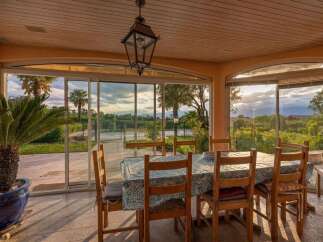 Enjoy breathtaking sunset views from this charming sunroom, featuring a dining table set for six and large glass windows that open to a lush landscape.