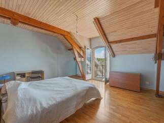 Discover this charming attic bedroom featuring exposed wooden beams and a sloped, wood-paneled ceiling that adds rustic character.