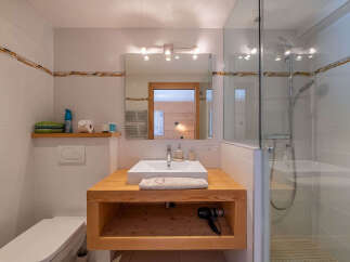 This modern bathroom features a sleek vanity with a wooden countertop and open shelving, perfect for storing toiletries.