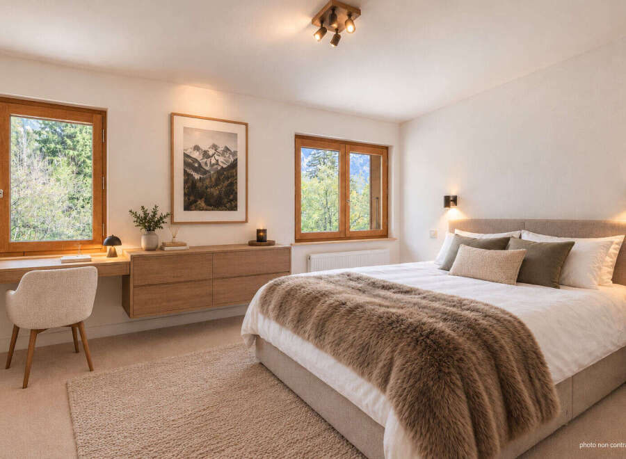 Experience serene mountain living in this beautifully appointed bedroom, featuring large wooden-framed windows that offer breathtaking views of the surrounding nature.