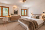 Experience serene mountain living in this beautifully appointed bedroom, featuring large wooden-framed windows that offer breathtaking views of the surrounding nature.