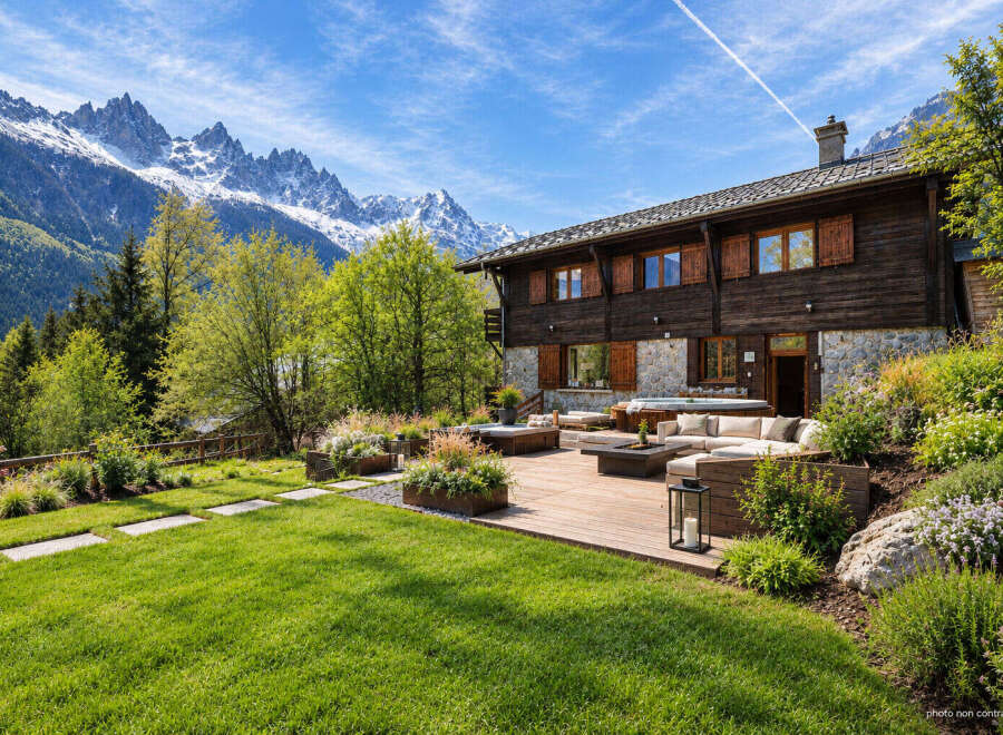 Experience luxury mountain living in this stunning chalet, featuring a spacious wooden deck with a hot tub and comfortable outdoor seating, perfect for enjoying the breathtaking alpine views.