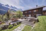 Experience luxury mountain living in this stunning chalet, boasting a spacious wooden deck with a dining area, comfortable lounge seating, and a relaxing hot tub.