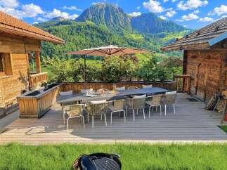 Experience breathtaking mountain views from this stunning wooden chalet's expansive deck, perfect for al fresco dining or relaxing under the large umbrella.