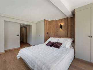 Experience modern comfort in this inviting bedroom, featuring a plush white bed adorned with decorative pillows and a warm wooden accent wall.
