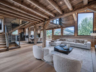 Experience luxury mountain living in this stunning chalet, featuring a spacious open-plan living area with a large sectional sofa and cozy armchairs.