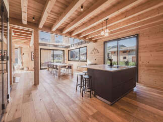 Experience modern mountain living in this stunning wooden chalet, featuring an open-plan living area with a sleek kitchen island and a spacious dining area.