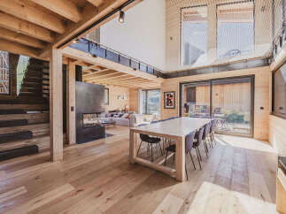 Experience modern mountain living in this stunning wooden chalet, featuring an open-concept living space with a sleek fireplace and a spacious dining area perfect for gatherings.